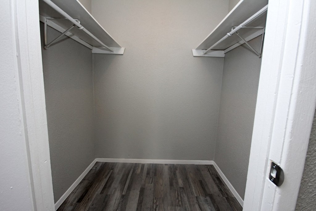 a walk in closet with two shelves and a wood floor