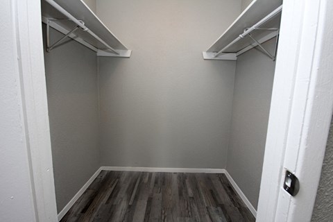 a walk in closet with two shelves and a wood floor