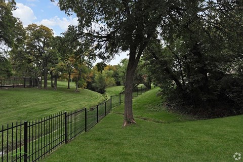 a wrought iron fence surrounds a grassy park with trees