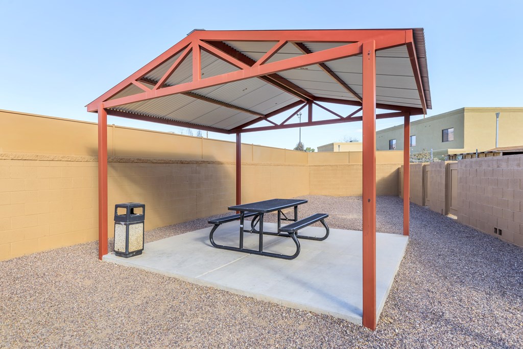 A picnic table is under a red canopy.