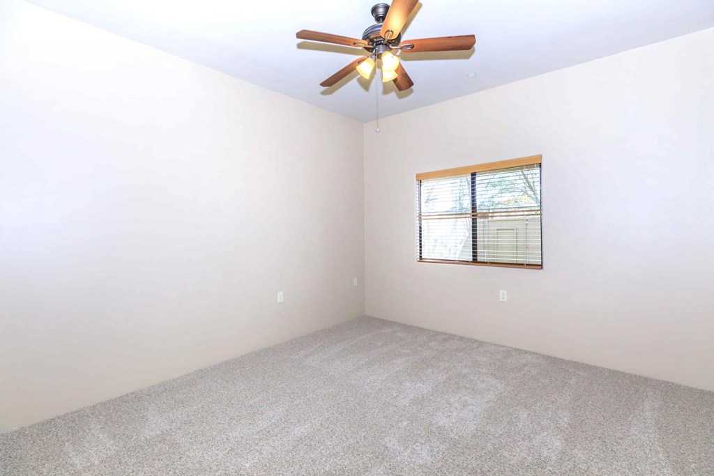 A room with a ceiling fan and a window with blinds.