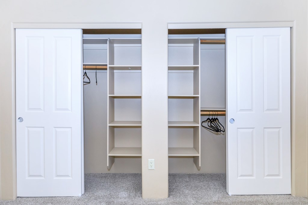 A white door is open to reveal a white closet with shelves and a coat hanging on a hook.