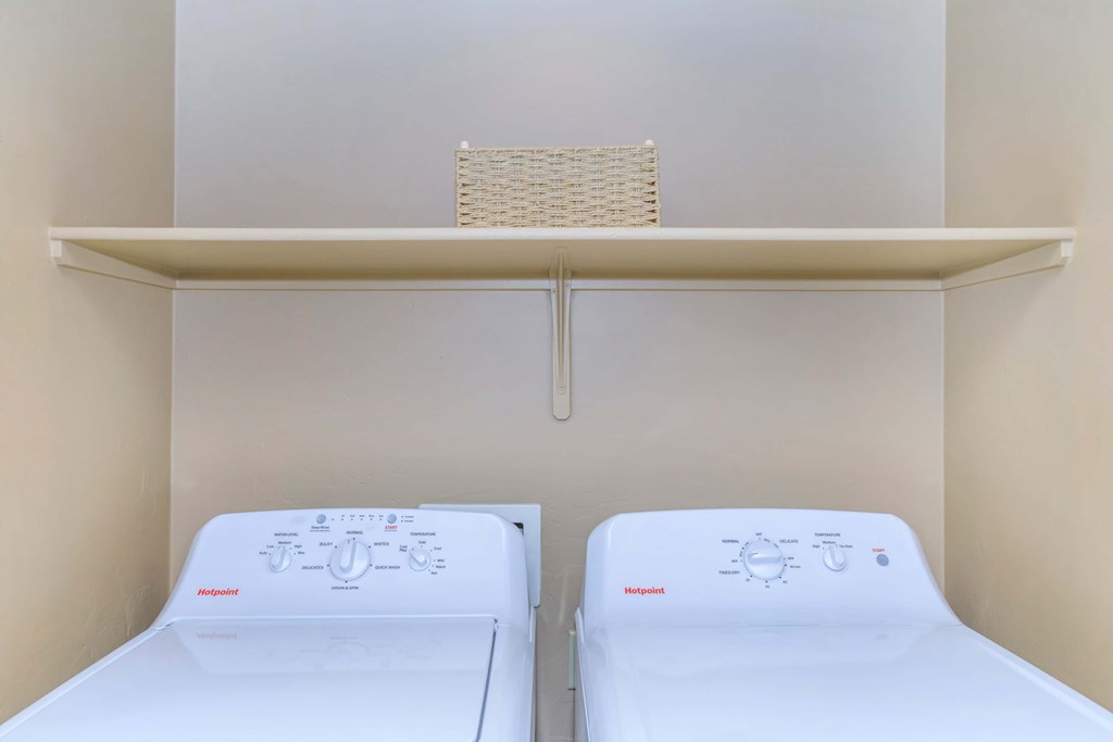 Two white beds in a small room with a shelf above them.