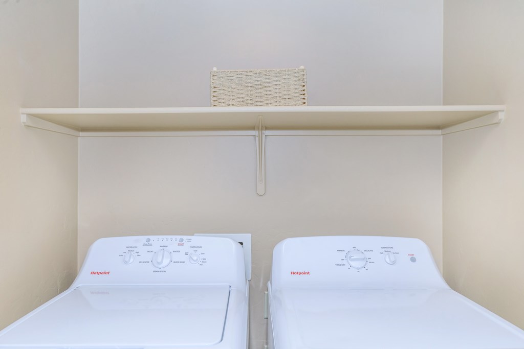 Two white beds in a small room with a shelf above them.