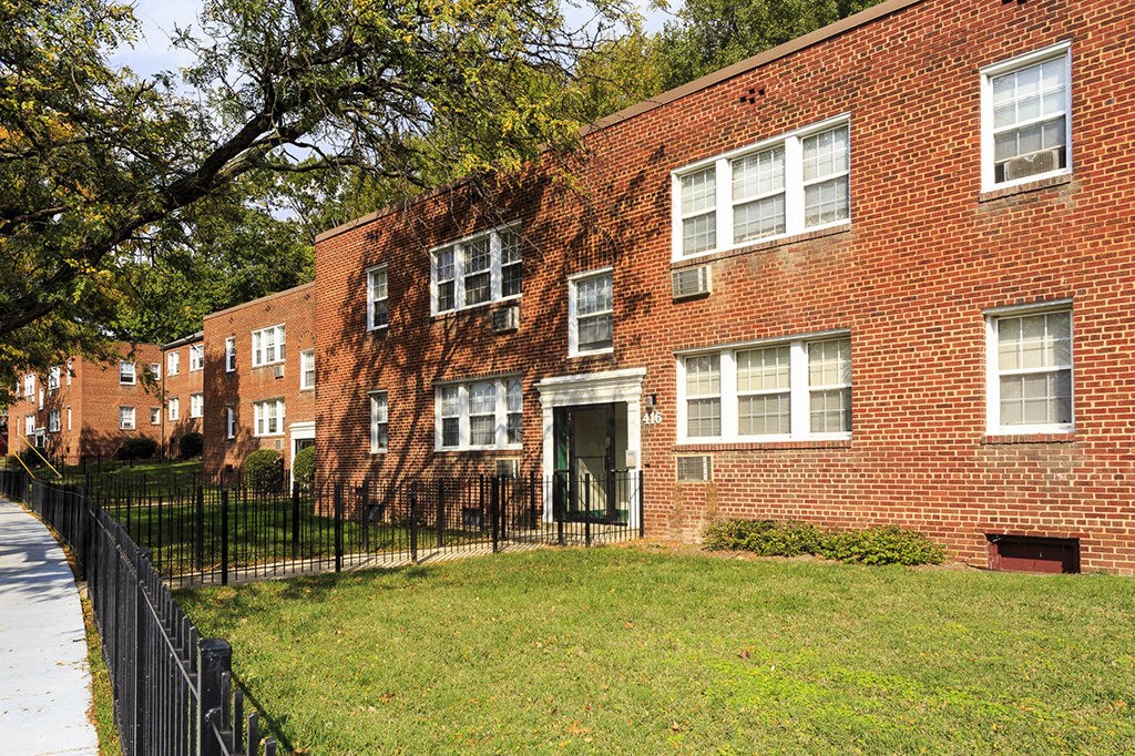 a brick apartment building with a yard and a wrought iron fence