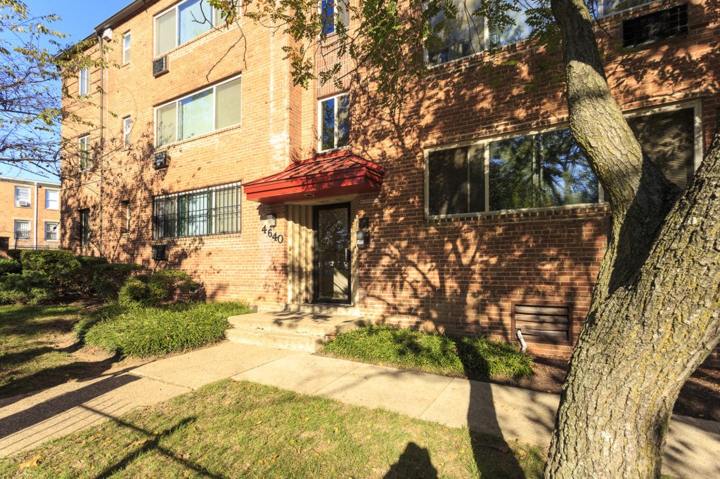 the front of a brick apartment building with a sidewalk and a tree