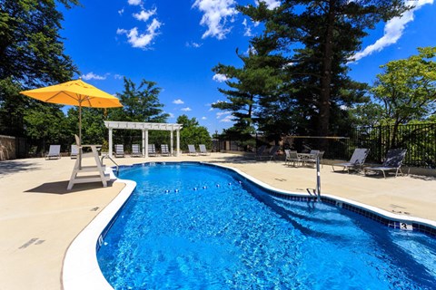 the pool is next to a patio with chairs and an umbrella