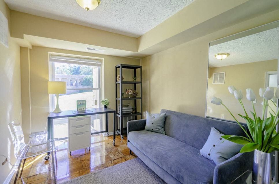 A living room with a grey couch, a table with a lamp, and a window.