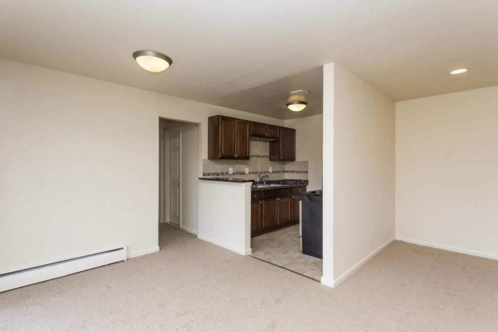 an empty living room with a kitchen in the corner