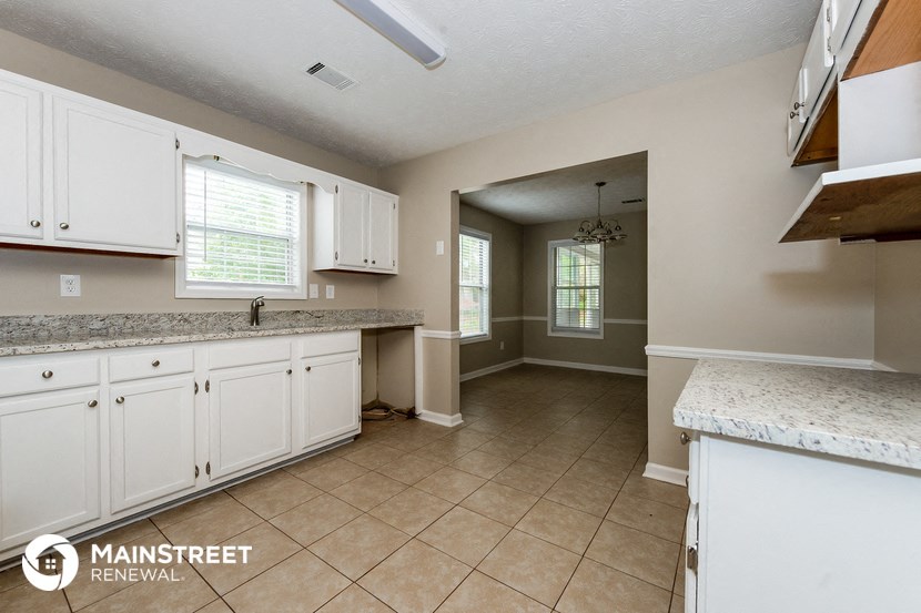a kitchen with white cabinets and tiled flooring and a door to a hallway