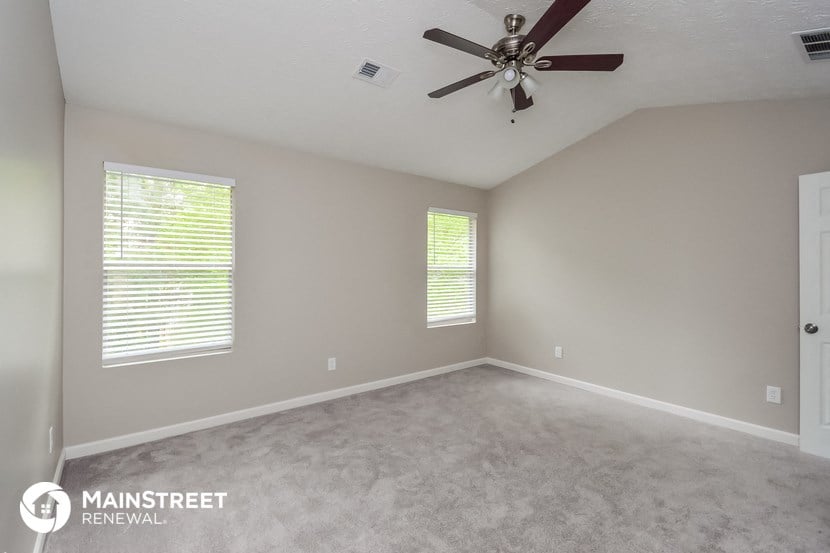 an empty room with a ceiling fan and two windows