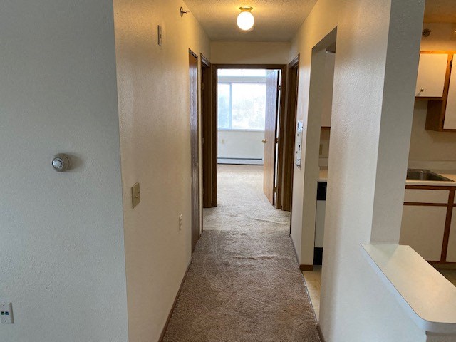 a hallway with a carpeted floor in a home with a door to a kitchen