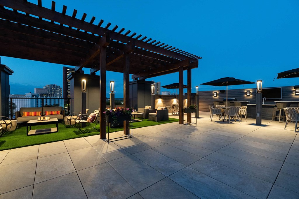 a rooftop terrace with patio furniture and a pergola at night