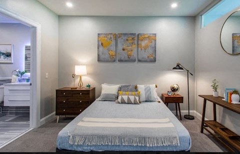 A bedroom with a large bed, a nightstand, a side table, and a painting on the wall.