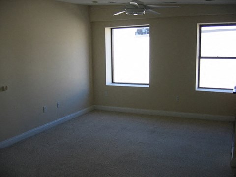 an empty room with two windows and a ceiling fan
