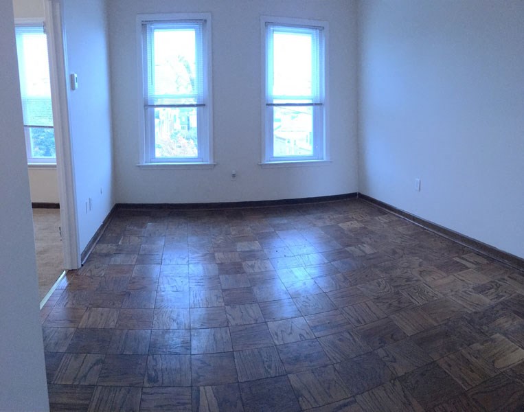 an empty room with a wooden floor and two windows