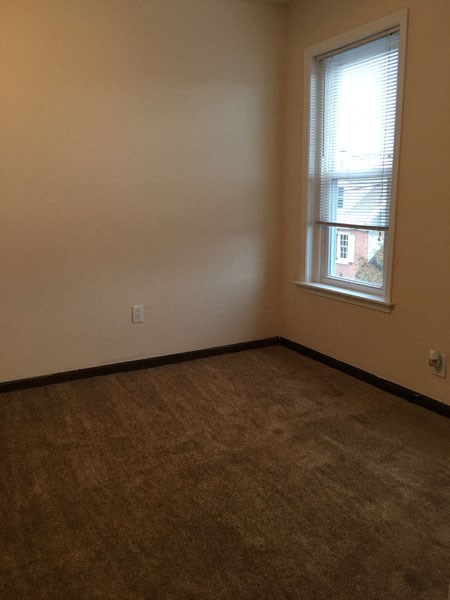 an empty room with a window and a brown carpet