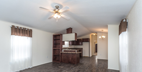 an empty living room with a ceiling fan and a kitchen