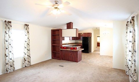an empty living room with a kitchen and a ceiling fan