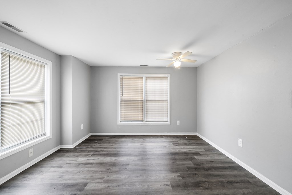 an empty living room with a ceiling fan and two windows
