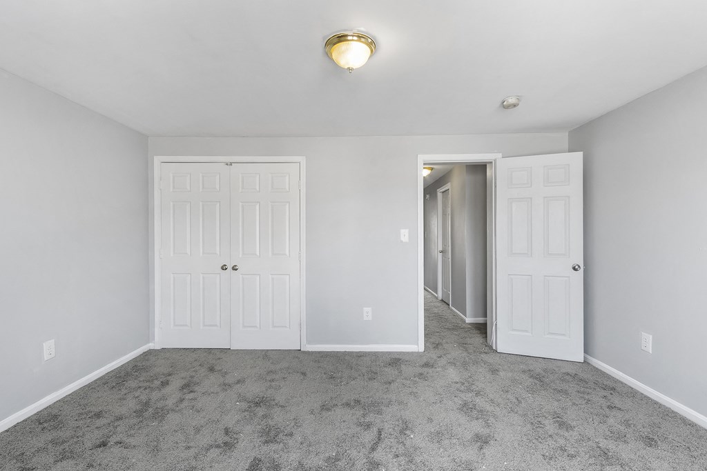 an empty bedroom with white doors and carpeting and a door to a hallway