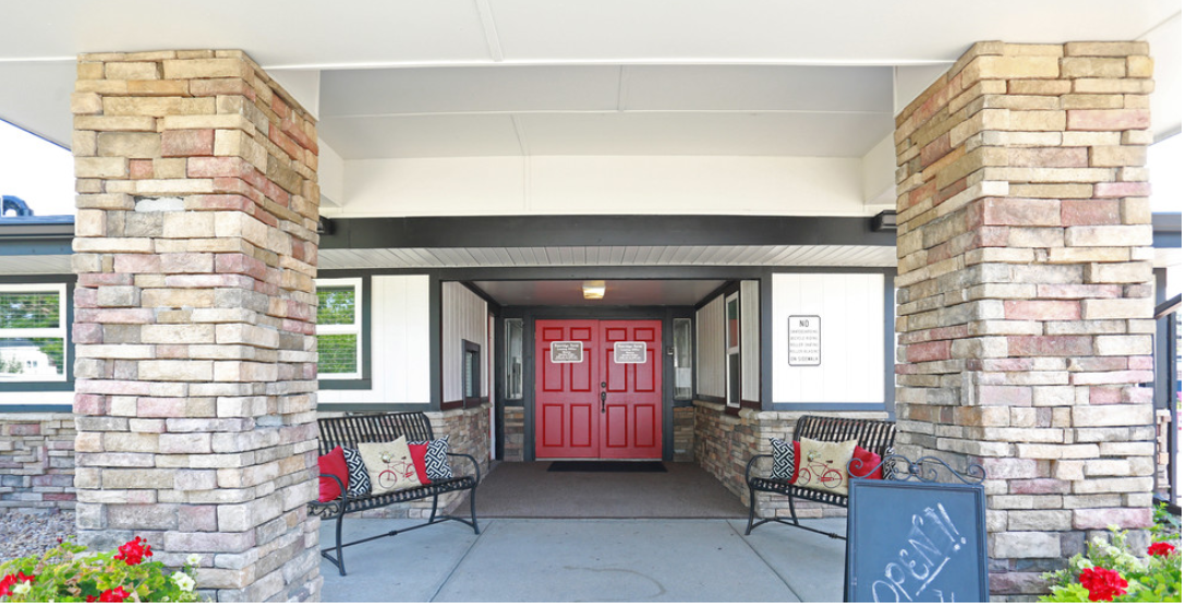 a red door on a building with a porch with two benches and a chalkboard sign