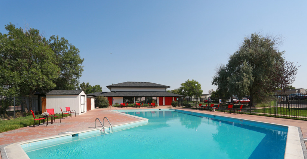 a swimming pool with red chairs around it and a white building in the background