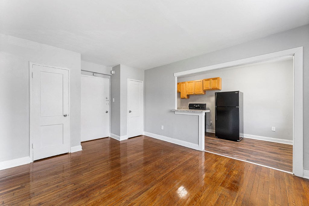 an empty living room with wood floors and a black refrigerator