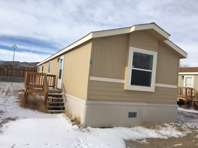 a small tan house with a porch and stairs in the snow
