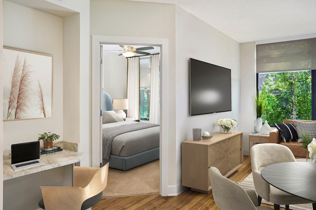 a living room with a bedroom in the background and a table with a laptop computer