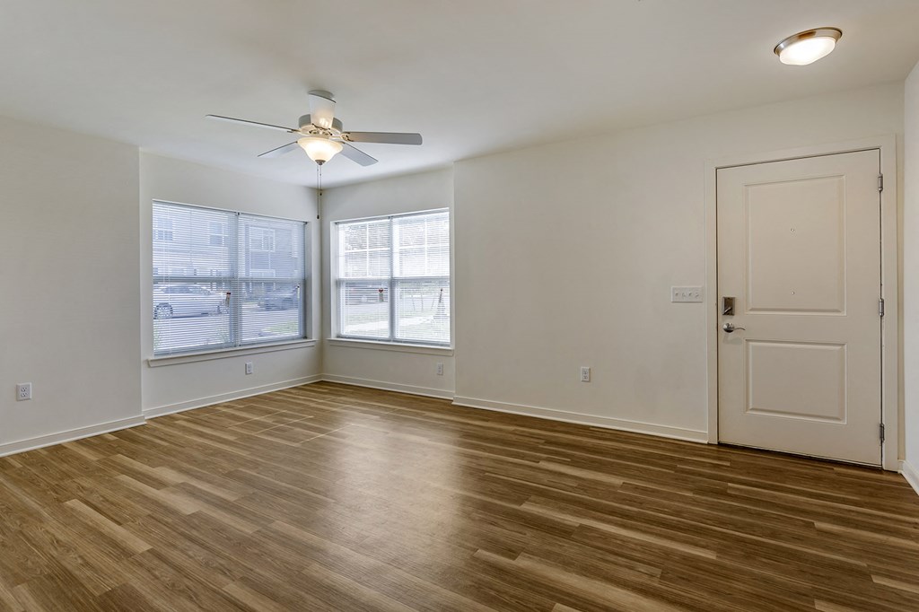 an empty living room with a ceiling fan and two windows