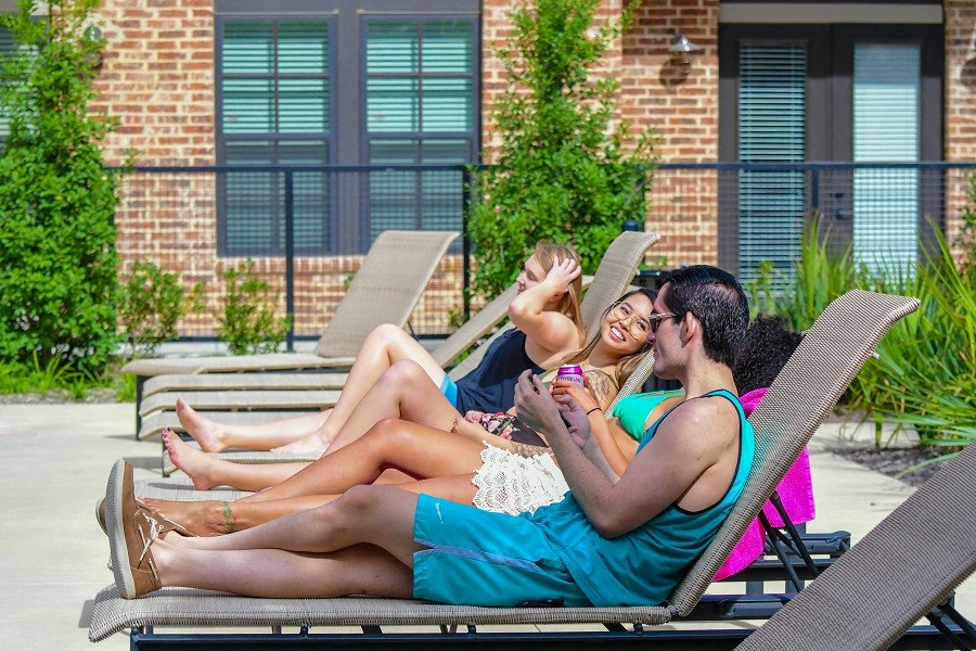 three women sitting on beach chairs talking and looking at their cell phones