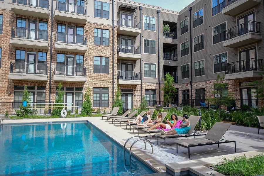 a group of people laying on chairs near a swimming pool in front of an apartment