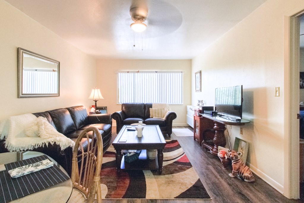 living room with ceiling fan, large window, hardwood-style flooring, and model furnishings