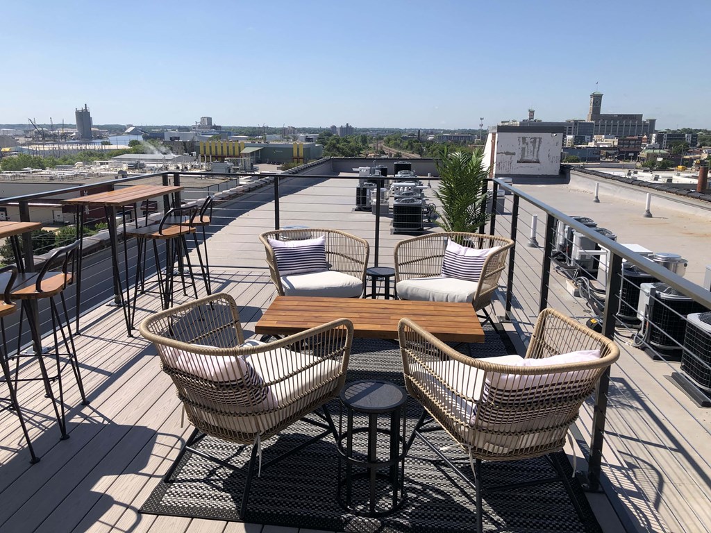 a rooftop patio with chairs and tables and a city in the background
