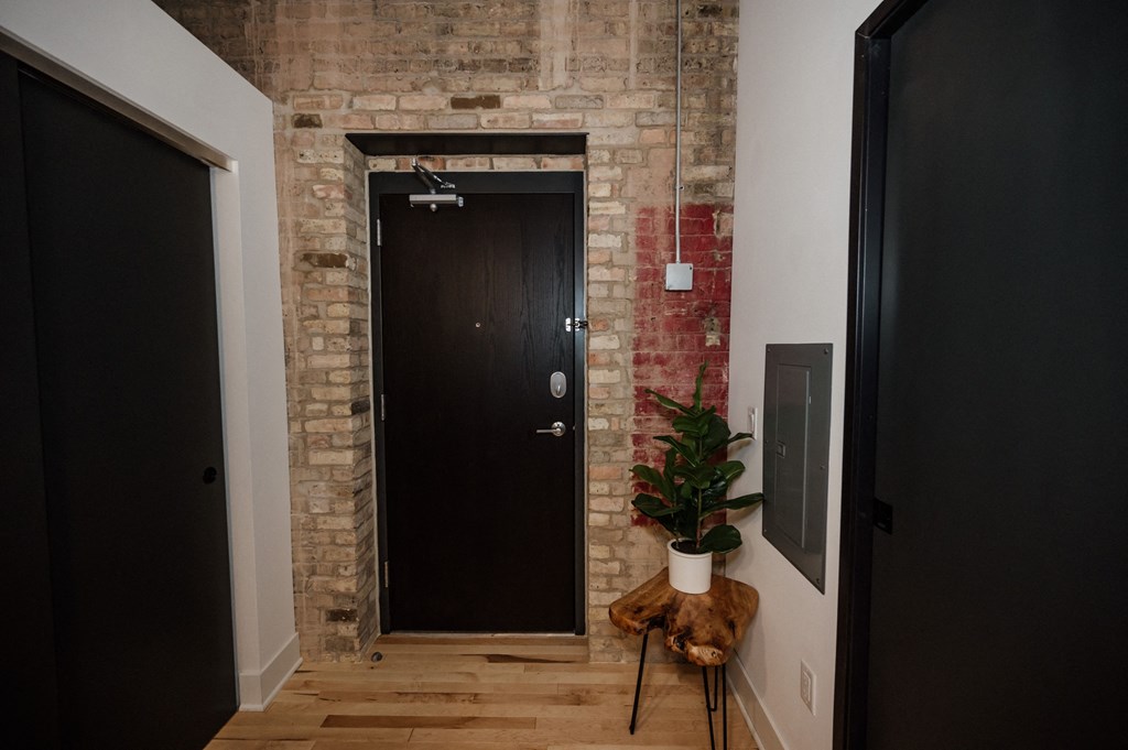 a brick wall with a black door and a plant on a stool
