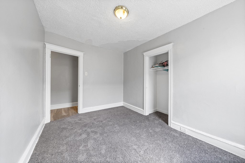 the living room of an empty house with a carpeted floor and an open closet