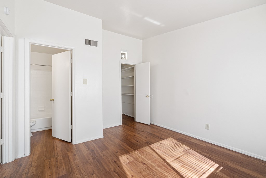 a bedroom with white walls and wood flooring and a closet