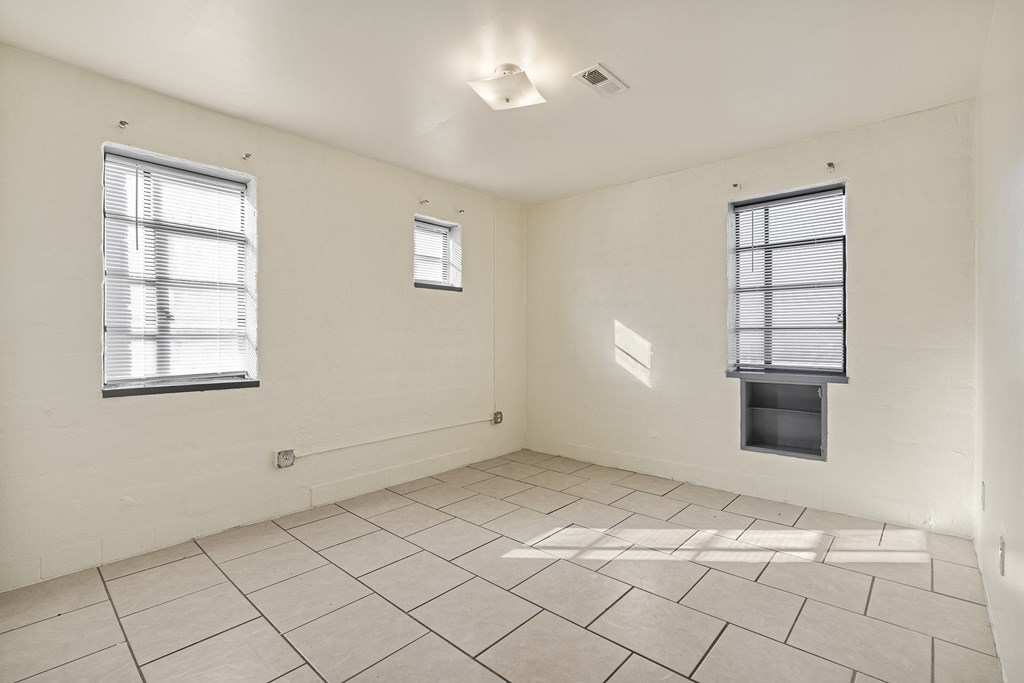 the living room of an empty apartment with two windows and a tiled floor