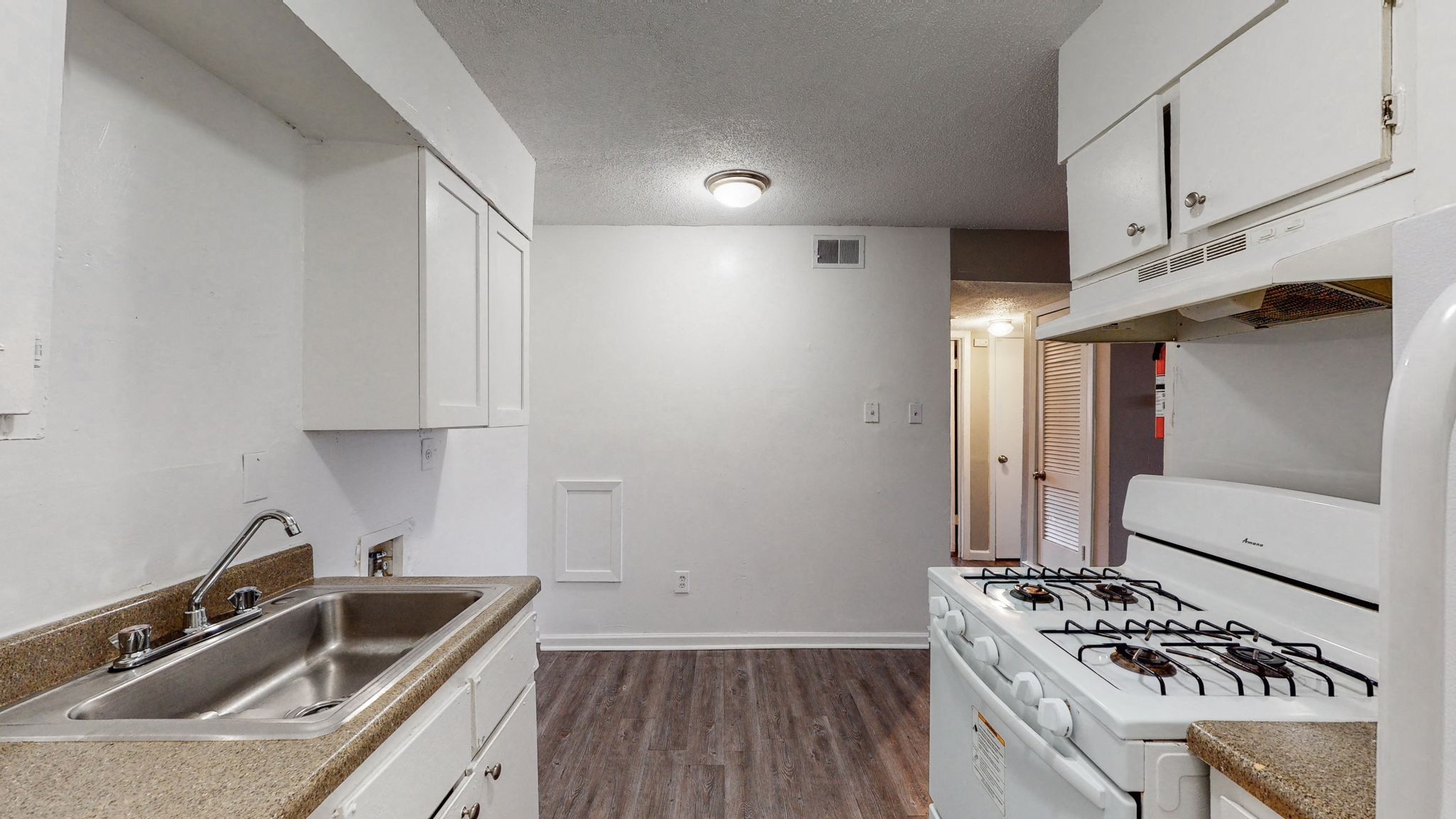 an empty kitchen with white appliances and a stove and sink