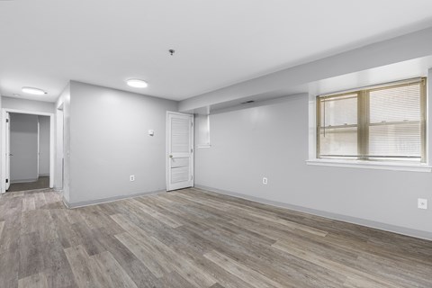 the living room of an apartment with white walls and wood flooring
