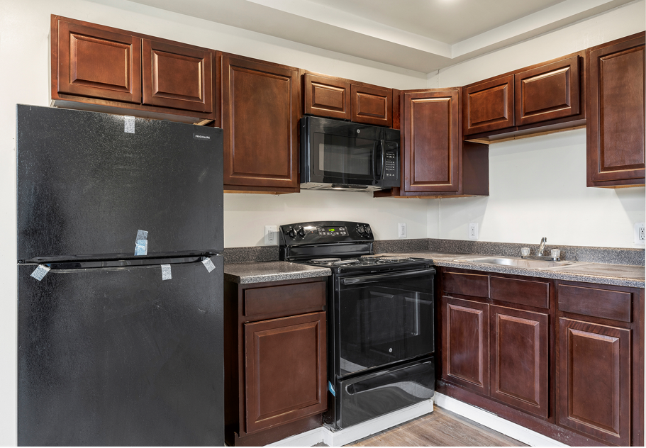 A black refrigerator is in a kitchen with brown cabinets.