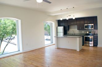 an empty living room with a kitchen and a large window
