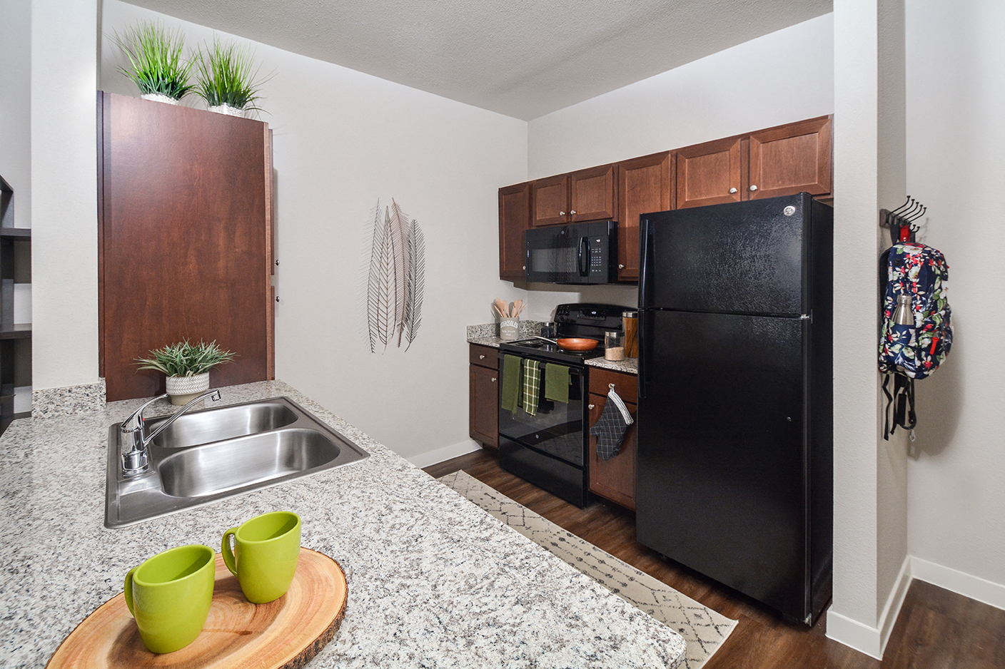 A kitchen with a black refrigerator and a sink with two green mugs on a wooden tray.