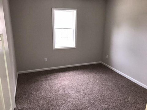an empty room with a window and gray carpet