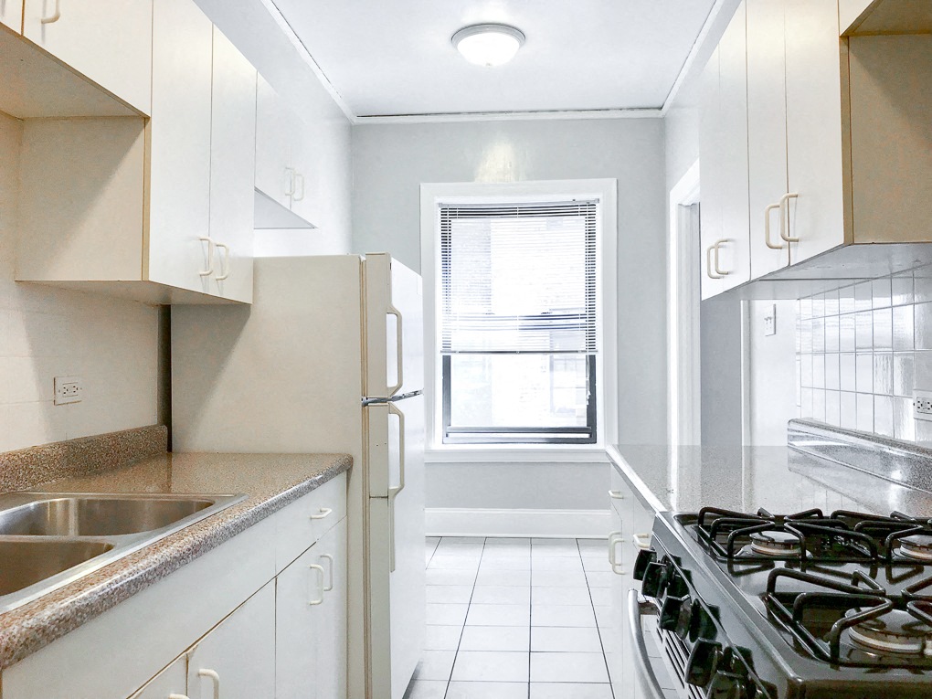 an empty kitchen with white cabinets and a window