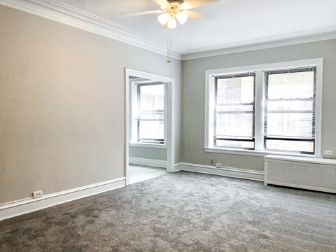 an empty living room with two windows and a ceiling fan