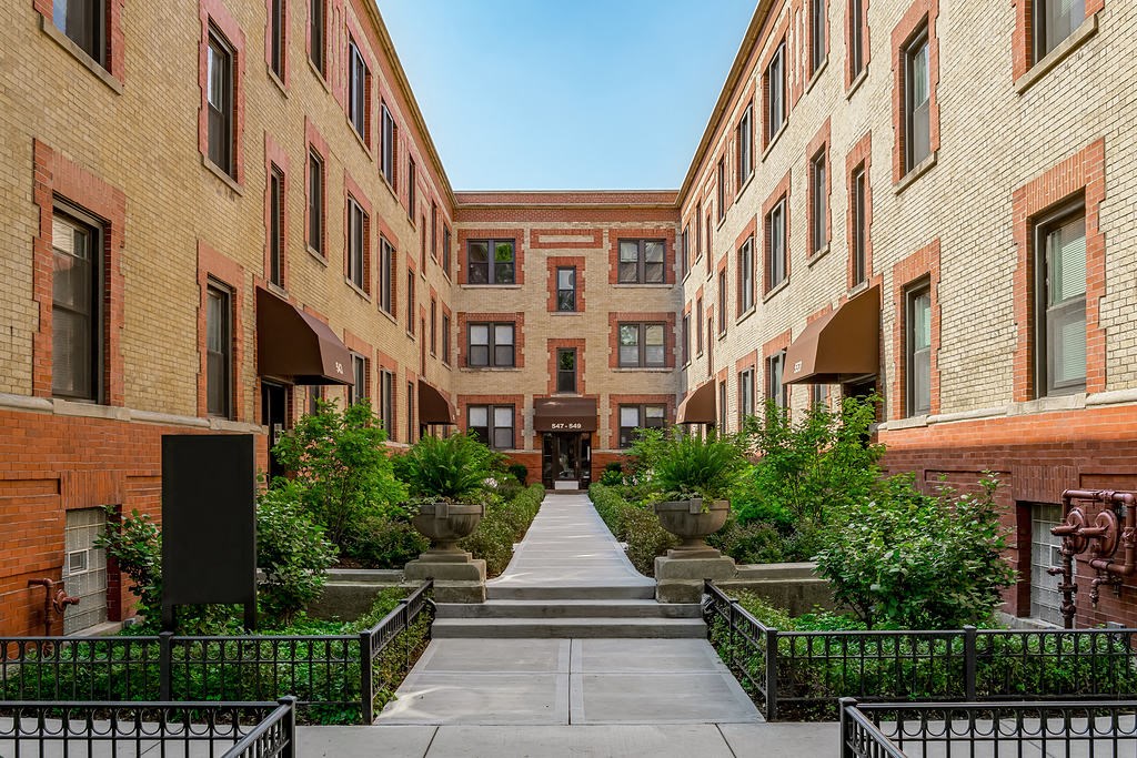 a courtyard between two tall brick buildings with trees and plants