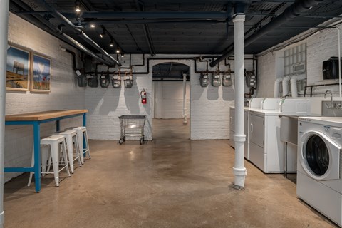 A laundry room with a washer and dryer, a table and stools, and a fire extinguisher mounted on the wall.
