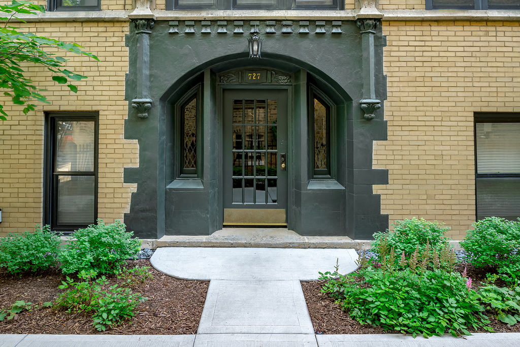 the front door of a building with a sidewalk and plants